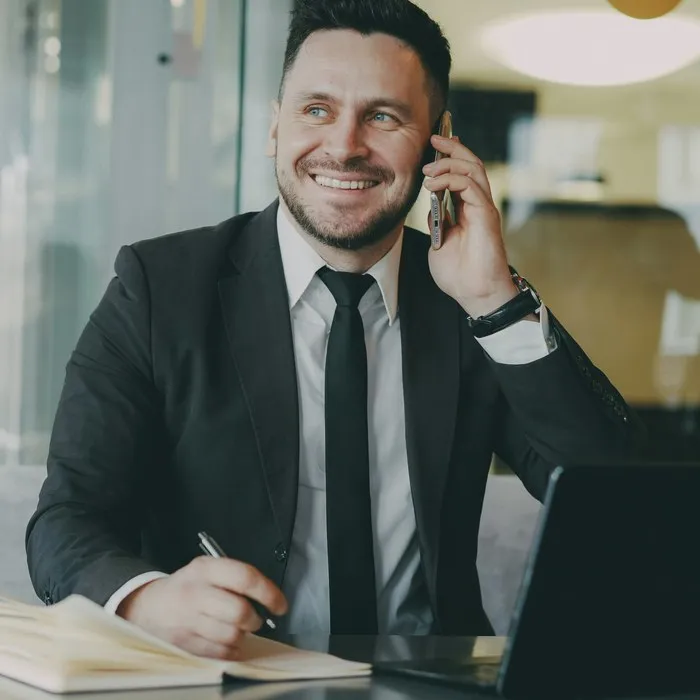 Un hombre sonriente con traje hablando por teléfono en su mesa